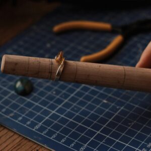 Close-up of an artisan shaping a handmade ring on a wooden mandrel tool.